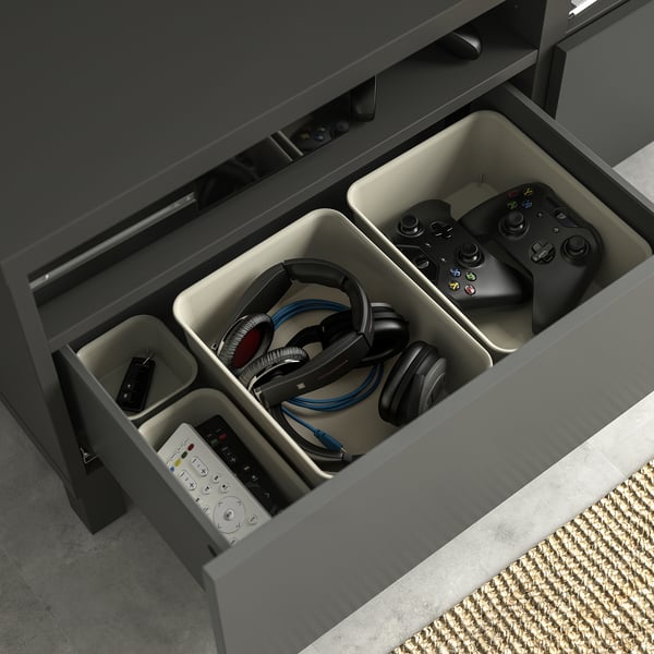 Open grey BESTÅ tv drawer, featuring organised gaming controllers, headphones, and remotes in compartments.