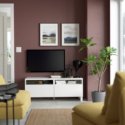 Modern living room with maroon walls, white BESTÅ tv stand, yellow armchairs, green plant, and landscape photos.