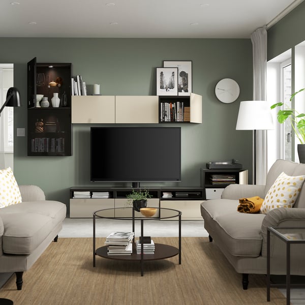 Modern living room with BESTÅ tv storage, grey sofa, flat-screen tv, glass coffee table, green wall storage, floor lamp, window, and clock.