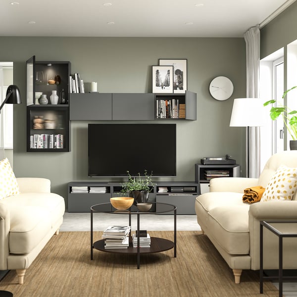 Modern living room with sage green walls, white sofas, glass coffee table, and black entertainment centre with tv, books, and decorations.