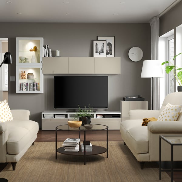 Modern living room with light furniture, large tv, sofas, coffee table, and plants.