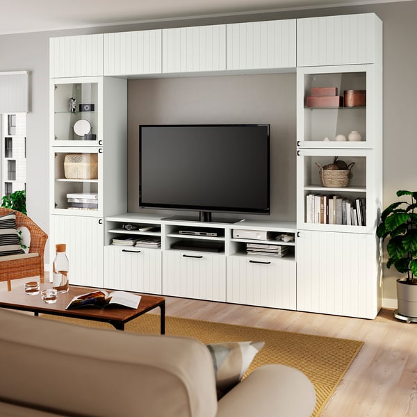 Modern living room with large white BESTÅ tv unit & flat screen. Light wood floor, beige couch, coffee table with decor. Right plant, left window.