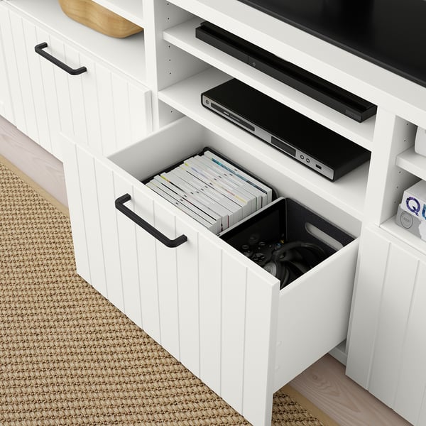 White BESTÅ tv unit with drawers open, revealing organised storage for electronics and magazines. Cable management seen at back.