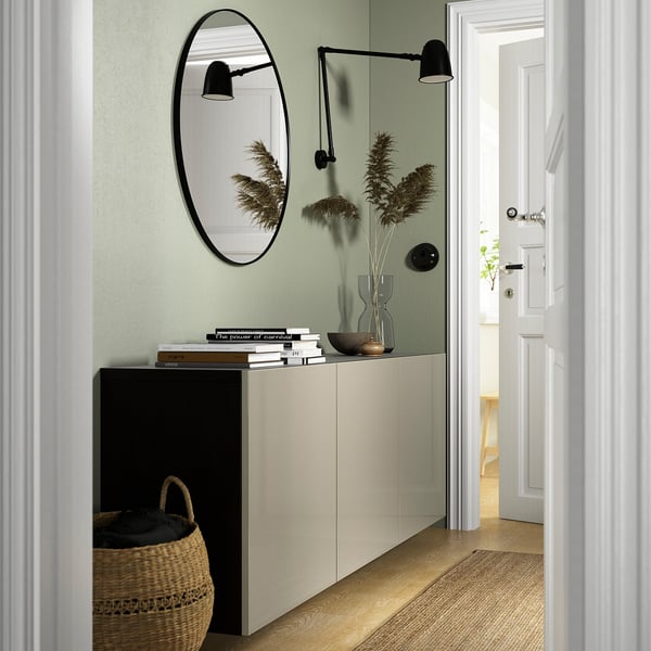 Modern hallway with BESTÅ white sideboard, black basket, round mirror, wall sconces, pampas grass flowers, and open door.
