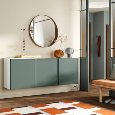 Modern entryway BESTÅ sideboard in green with glossy white top. Round mirror above, decorative vase and lights add style. Wooden bench nearby.
