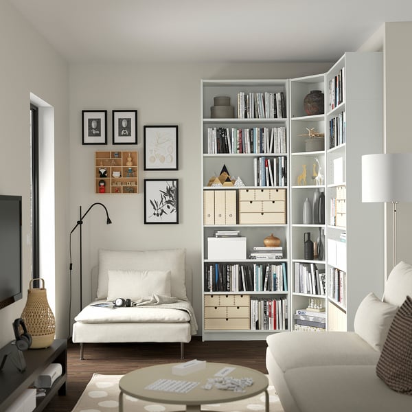 Modern living room with white BILLY bookcases, a white sofa, and a black floor lamp. The bookcases have books, vases, and decorative items.