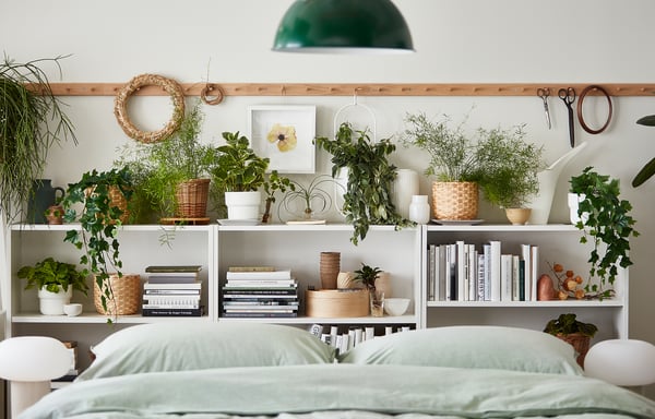 Bedside: white BILLY bookshelf with green plants, books, and wicker basket decor. Green bedding underneath.
