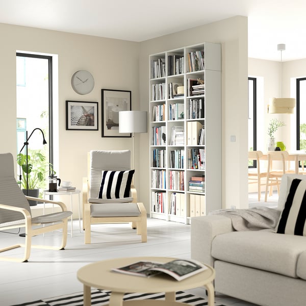 Modern living room with light furniture, BILLY bookcase, white couch & chairs, coffee table, large windows.