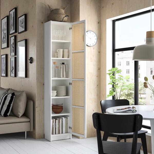 Modern living room with white BILLY bookcase, bamboo doors, black chairs, grey sofa, natural decor by large window.