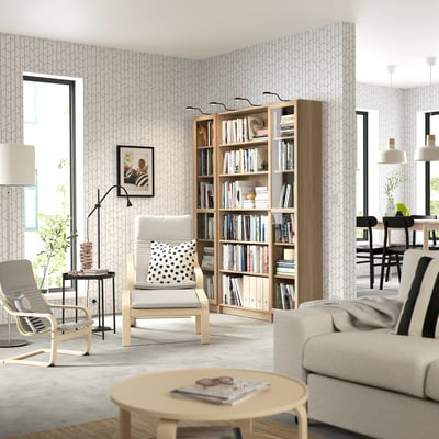 Modern living room with bookcase, sofa, armchairs, and lamp.