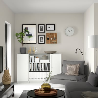Modern living room with white BILLY bookcase, grey sofa, coffee table, plant, and wall clock.