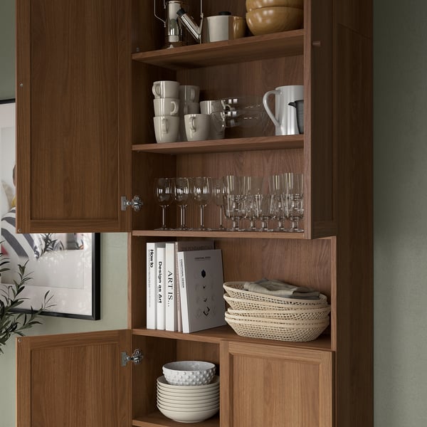 Wooden open cabinet displays mugs, glasses, plates, and baskets. Adjustable shelves customise storage, fitting various kitchen and dining items.