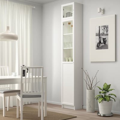 Minimalist dining area with white BILLY cabinet displaying items, next to a white chair & table under a hanging lamp.