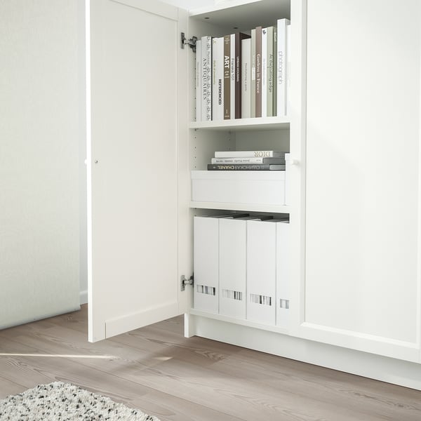 A white BILLY bookcase stands against a wall, storing stacks of books on open shelves and closed panels below.