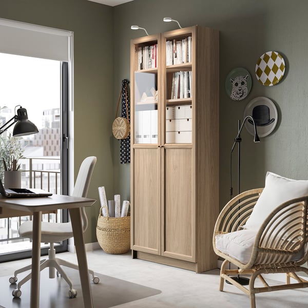 Cosy home office with BILLY bookcase, wicker chair, lamp & vase. Natural light, calm atmosphere.
