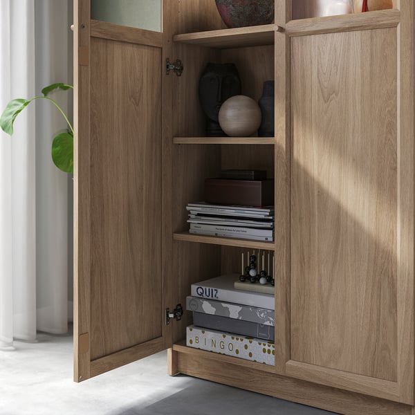 Wooden bookcase with glass doors showing shelves stocked with books, decor items, and games, demonstrating versatile storage and display capabilities.
