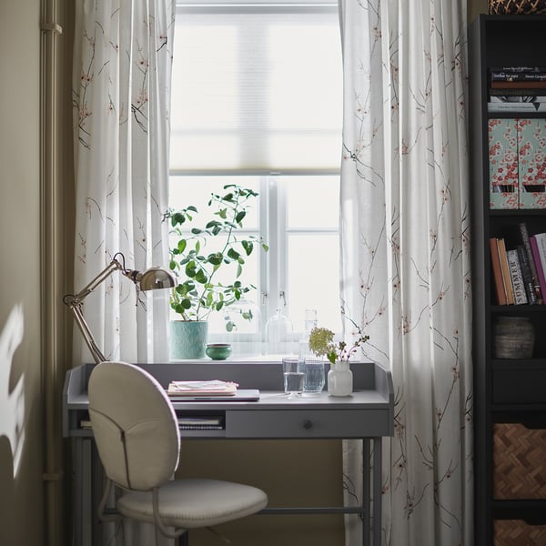 Cosy home office with grey BJÖRKBERGET chair, white curtains, desk, lamp, and plant.