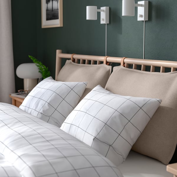 Cosy bed with adjustable pillows, dark green wall, flanked lamps, bedside table with lamp and plant.