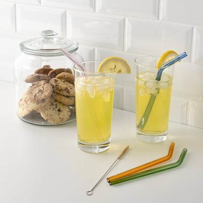 Two glasses with lemon drinks, colourful glass straws, and a cookie jar on a tiled surface.