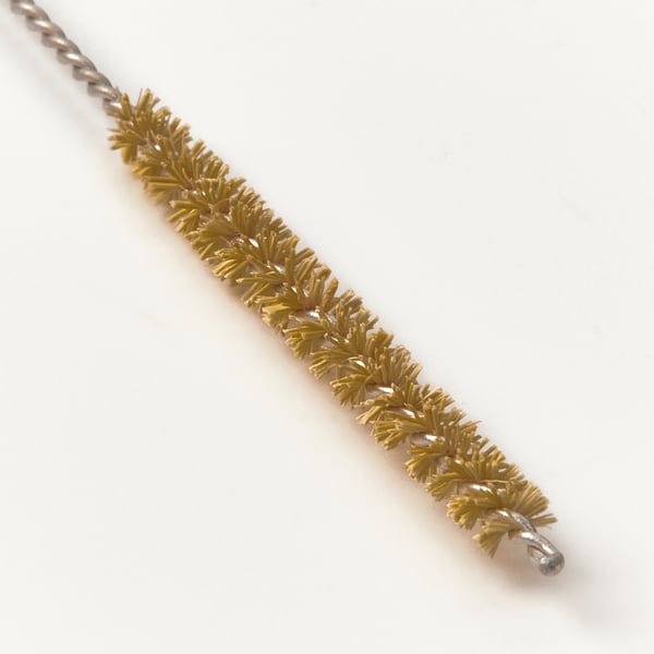 Closeup of gold-colored cleaning brush with wire handle, bristles detailed.