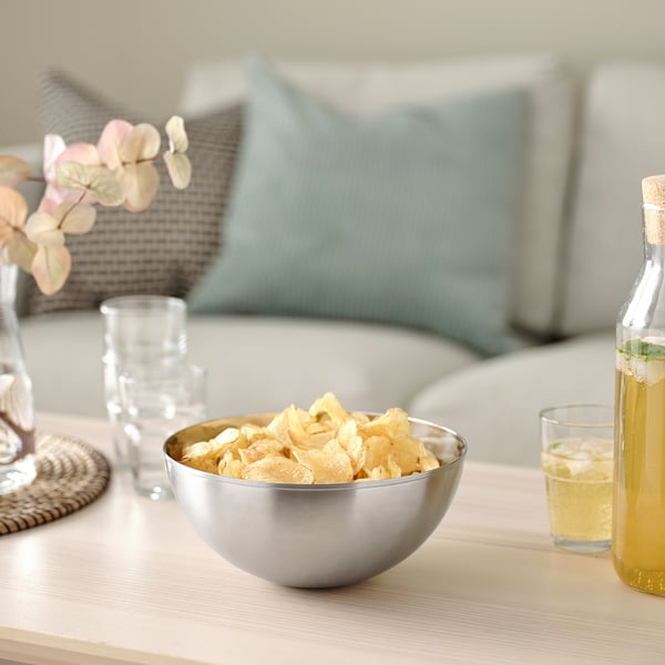Silver bowl with chips on wooden table, beside glasses, bottle, and vase.