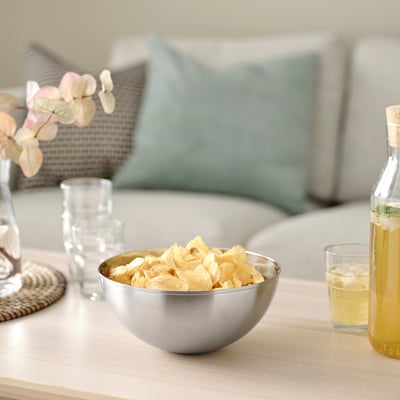 Silver bowl with chips on wooden table, beside glasses, bottle, and vase.