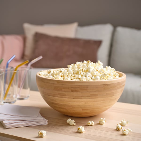 Large wooden bowl filled with popcorn sits on a coffee table near glasses and cushions.