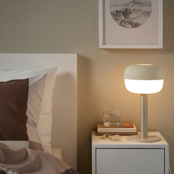 Bedside with BLÅSVERK lamp, white pillows, glass, & books.