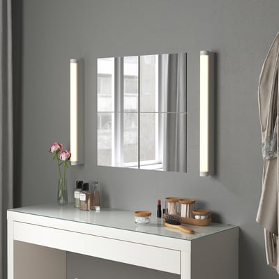Summation: a modern bathroom the BLODLÖNN mirror trio in silver, flanked by lit sconces, atop a white vanity with toiletries and pink roses.