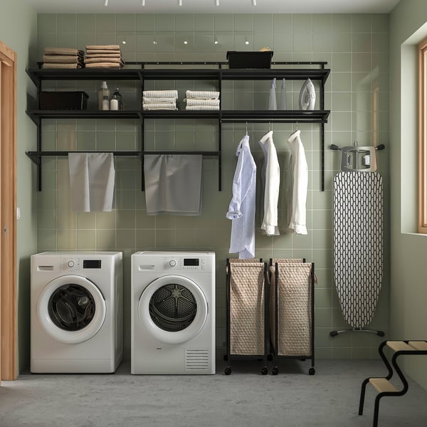 Modern laundry room with BOAXEL dark grey wall storage, ironing board, machines, and wicker baskets.