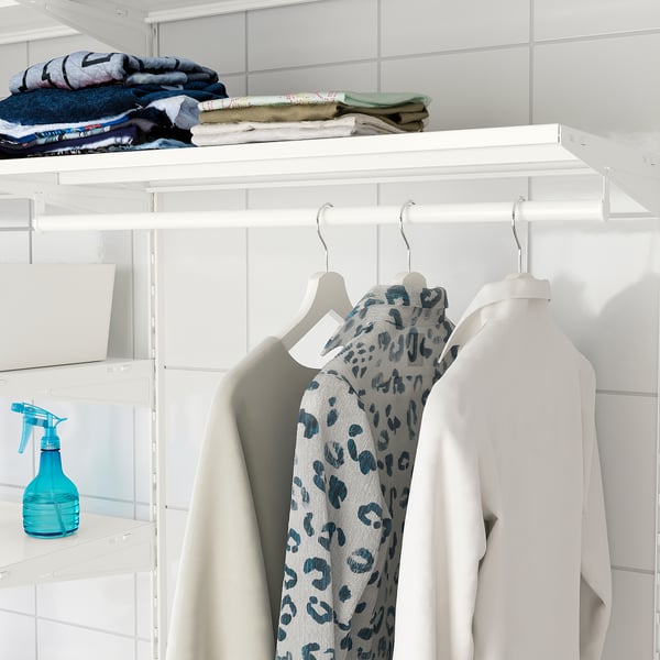 White closet with shelves storing folded clothes and hanging garments, including a patterned top and sweater.