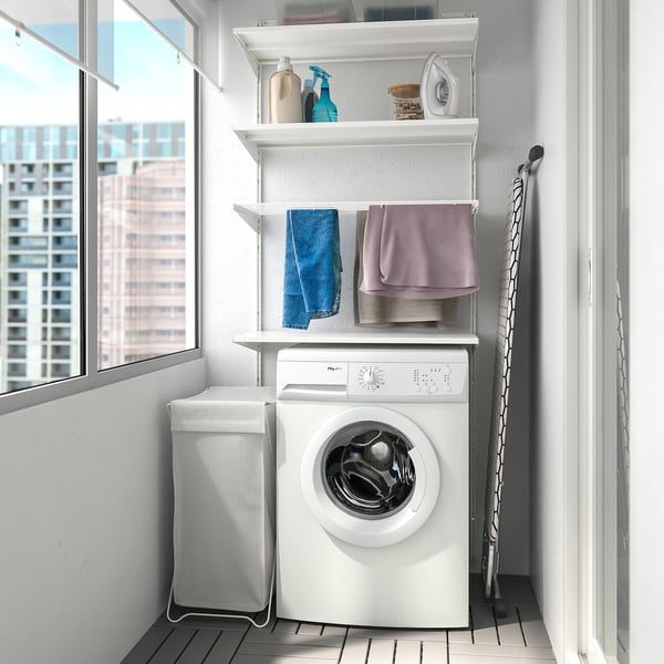 Laundry corner with white shelves, towels, machine, basket, ironing board, window.