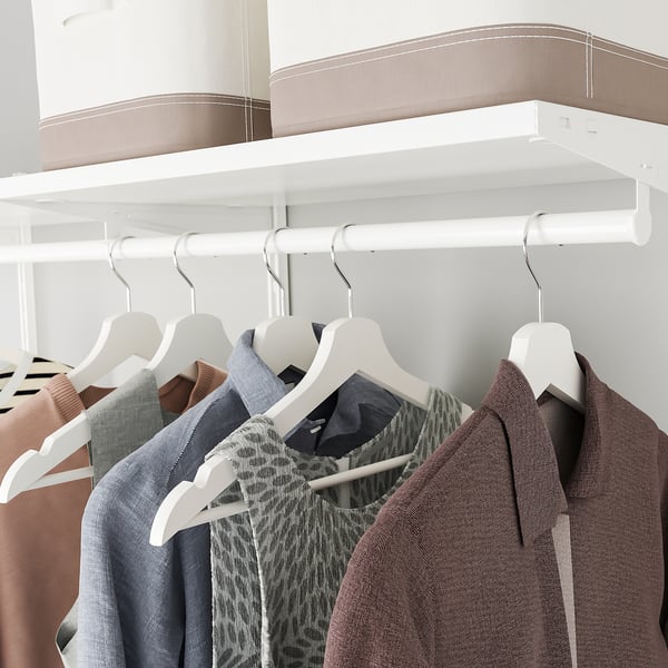 Organised wardrobe with white hangers and shelves. Clothes hang neatly, showcasing efficient storage.