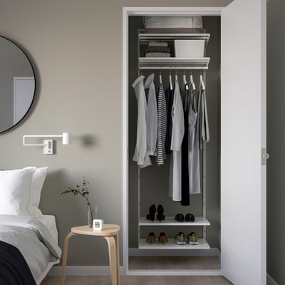 Open closet BOAXEL in white, hanging clothes, shoes below, shelved items above. Compact closet fits neatly beside bed.