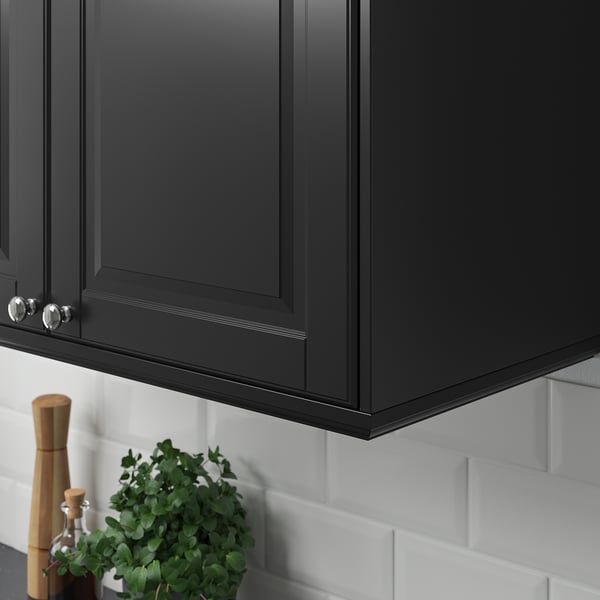 Black kitchen cabinets with silver handles and a white tiled backsplash; a potted plant and a wooden pepper grinder are placed beneath the cabinets.