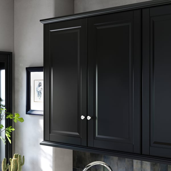 Black kitchen cabinets, sleek and modern, with smooth lacquered doors and silver knobs, mounted on a wall with a grey backsplash.