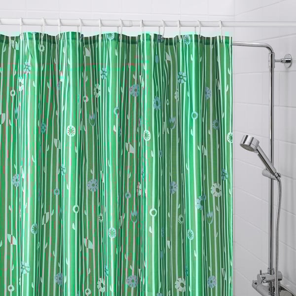 Green shower curtain BOLLBUDDLEJA with small flowers hangs in bathroom, covering entire shower area, with metallic shower head visible on right.