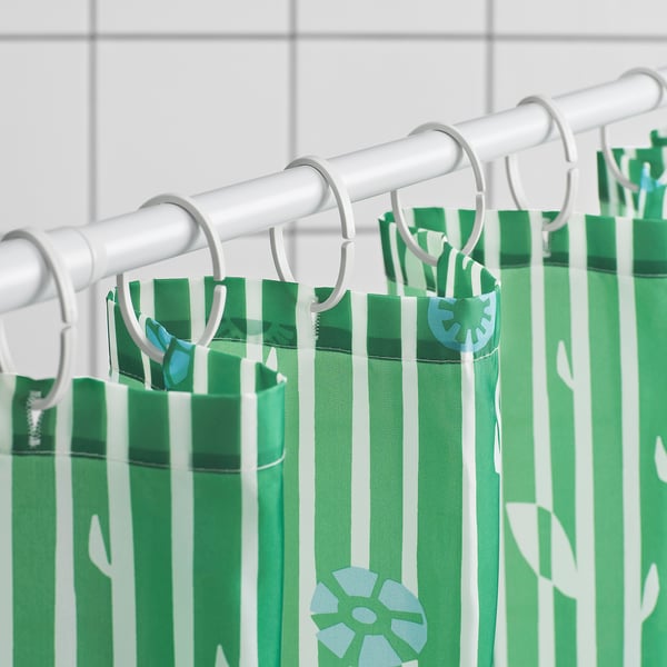 Green striped shower curtain with white flowers hangs by rings from a rod, water-repellent surface.