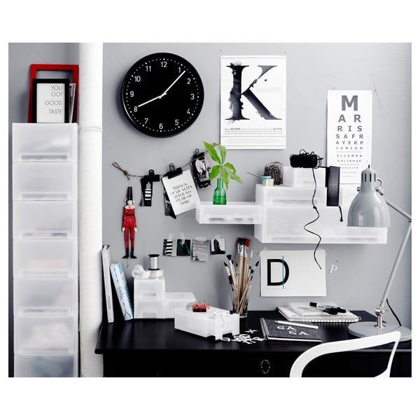 Modern desk space with black desk, white shelves, clock, lamp, and decorative items including a red figurine and green plant.