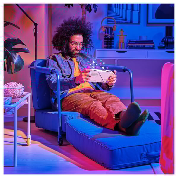 Person reclines in blue BRÄNNBOLL lounge chair, reading with feet up, beside popcorn.