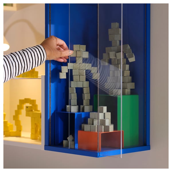 Hand adjusts cubes in blue ikea cabinet with transparent panels.
