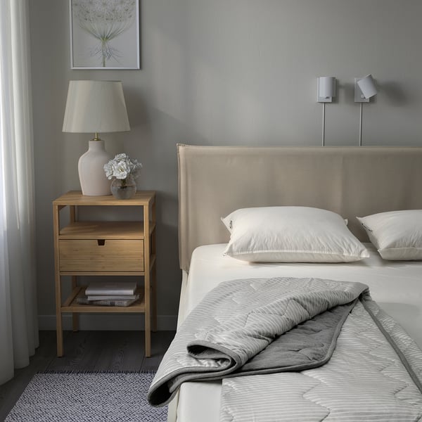 Modern bedroom with BRANDLILJA duvet on bed, bedside table, lamp, flowers. Calm, neutral colours.