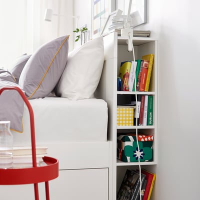 White BRIMNES headboard with shelves holding colourful books and a red bedside table with a vase.