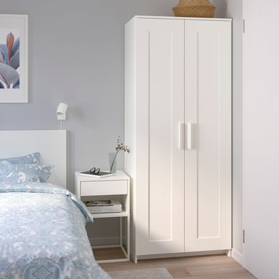 Tall white BRIMNES wardrobe beside bed in small bedroom.