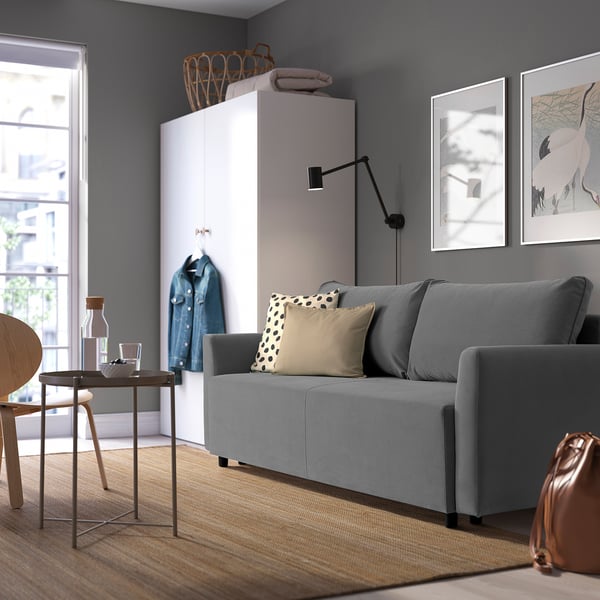 Modern living room with BRISSUND sofa bed, cushions, white cabinet, art, coffee table, and decor.