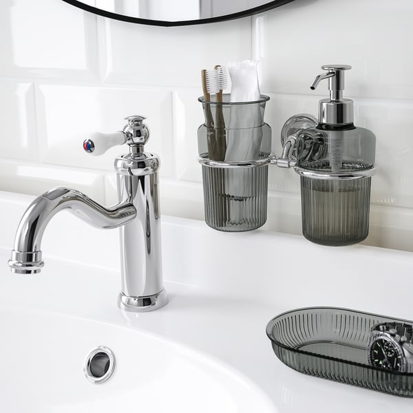Chrome-plated sink tap with gleaming finish, accompanied by matching soap dispenser and toothbrush holder on wall, all part of brofjäreden series.