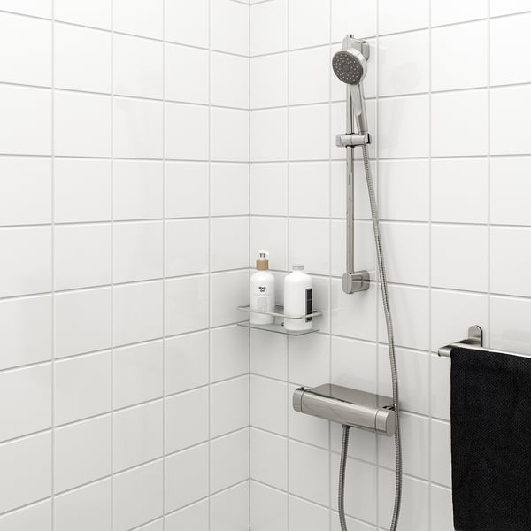 BROGRUND shower system with chrome finish, riser rail, handheld shower, black towel, toiletries shelf in white-tiled shower.