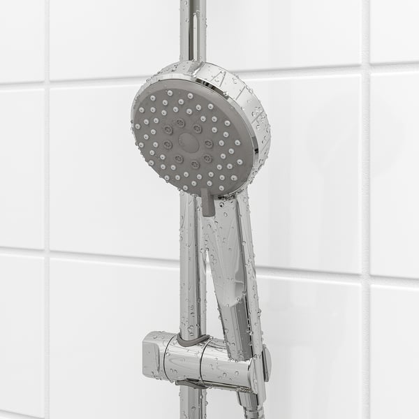 Chrome shower head with multiple spray holes, likely part of BROGRUND set, shown against tiled wall, wet from use.