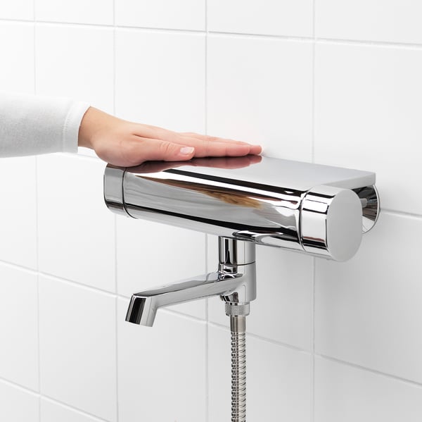 Hand adjusts modern shower mixer with safety stop and cold touch feature. Chrome finish, mounted on tiled wall.