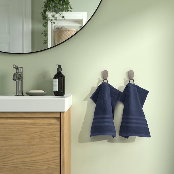 Blue BROKGLIM towels on hooks near modern sink with mirror. Organic cotton, elegant border. Green walls, wooden cabinet. Clean, contemporary design.